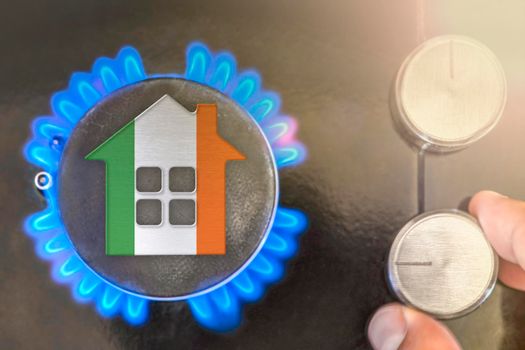 Heating season or gas use in Ireland. Concept, model of a house stands near the flame of a gas boiler on a black background. The cost of using natural gas in Ireland