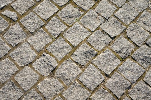 Chipped stone pavement background texture, cobbled street in sunlight.