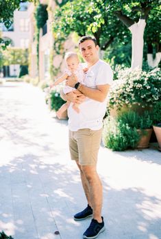 Smiling dad with a little girl in his arms stands on the street near flower pots. High quality photo
