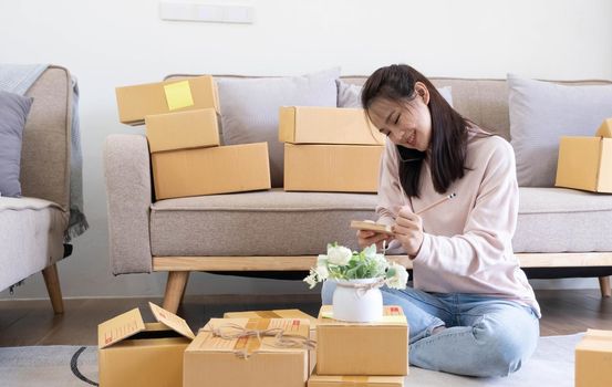 Young attractive asian woman owner startup business look at camera work happy with box at home prepare parcel delivery