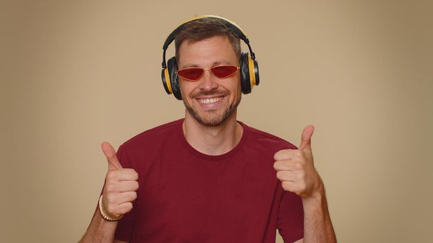 Happy handsome relaxed man with purple coiffure hairstyle listening music via headphones and dancing disco fooling around having fun expressive gesticulating hands. Adult stylish male guy indoors