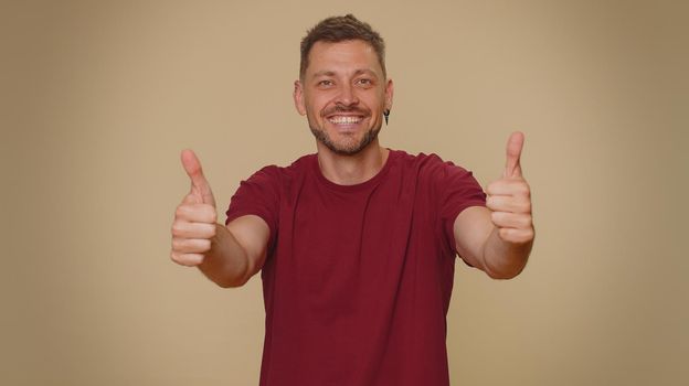 Like. Bearded handsome young man raises thumbs up agrees with something or gives positive reply recommends advertisement likes good. Adult stylish guy isolated alone on beige studio background indoors