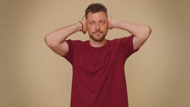 Dont want to hear and listen. Frustrated annoyed irritated handsome young man covering ears, gesturing no, avoiding advice ignoring unpleasant noise loud voices. Adult stylish guy on beige background