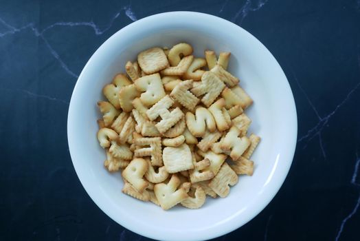 letter shape sweet cookies in a white bowl on black ,