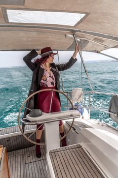 Attractive middle-aged woman at the helm of a yacht on a summer day. Luxury summer adventure, outdoor activities