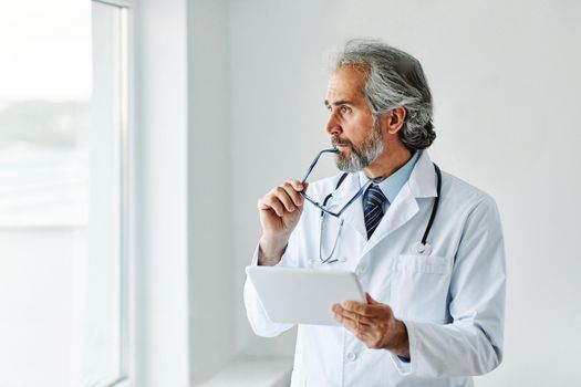 portrait of a senior doctor holding a tablet computer in his office in a hospital