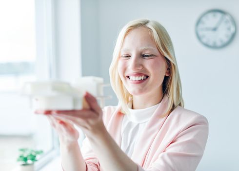 portrait of a young business woman holding a modern house model in the office