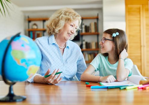 grandmother teaching granddaughter and helping her with homework and coloring book at home