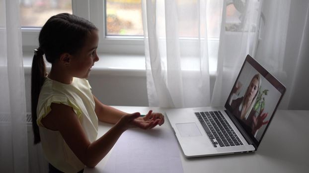 Pretty primary school girl distance learning at home. Focused cute kid listening audio lesson studying at table, doing homework. Children remote education on quarantine concept.