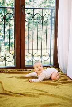Smiling baby lies on his tummy on a blanket on the floor near the balcony door. High quality photo