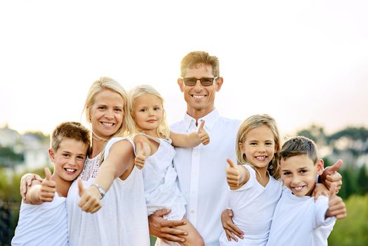 Thumbs up if you love your family. a happy family with their thumbs up outdoors