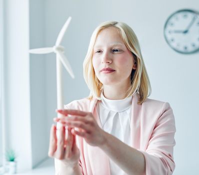 portrait of a young business woman holding a windmill model in the office