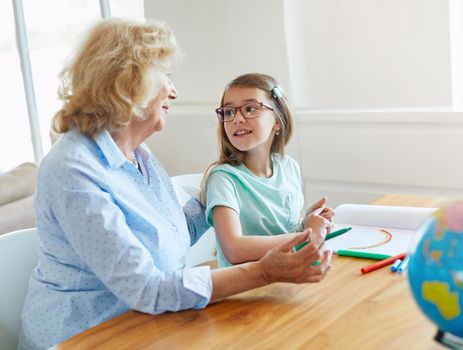 grandmother teaching granddaughter and helping her with homework and coloring book at home