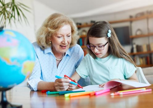 grandmother teaching granddaughter and helping her with homework and coloring book at home