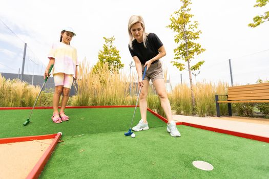 mother and daughter playing mini golf, children enjoying summer vacation.