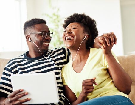 Portrait of a lovely young couple having fun and listening music wearing earphones and holding tablet together at home
