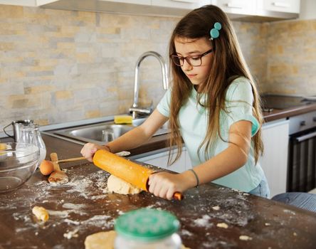 Happy little girl making dough in the kitchen at home