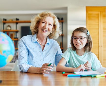 grandmother teaching granddaughter and helping her with homework and coloring book at home