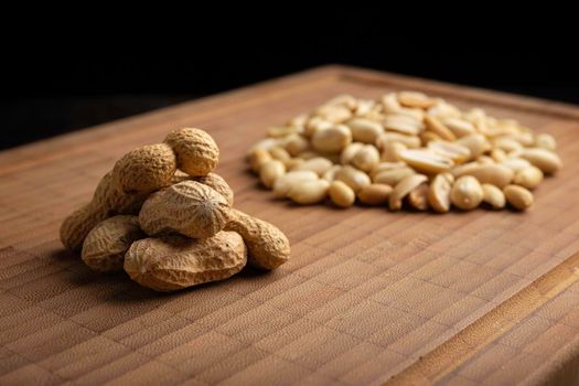 peeled and unpeeled peanuts seeds and on bamboo cutting table with black background. (arachis hypogaea) Edible seeds. Healthy snack nutrition concept