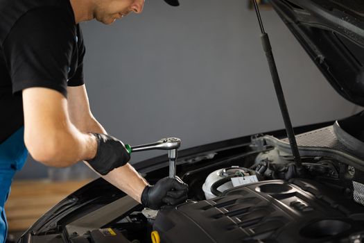 Close Up of male mechanic working on car in a Car Service. Empowering man makes an usual car maintenance. He's using a ratchet. Modern clean workshop. Auto service.