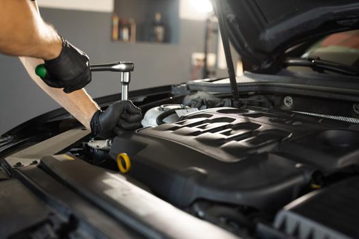 Close Up of Male Mechanic Working on a Car in a Car Service. Empowering Man Makes an Usual Car Maintenance. He's Using a Ratchet. Modern Clean Workshop. Auto Service.