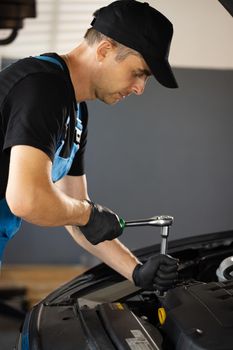 Car mechanic using wrench to repair the engine, car service. Auto service. Empowering male mechanic is working in car service. Man is working on an usual car maintenance. He's using ratchet.