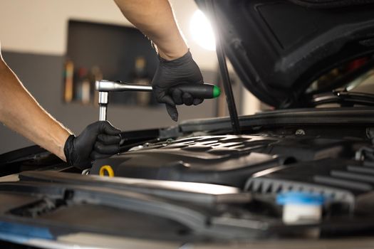 Close Up of Male Mechanic Working on a Car in a Car Service. Empowering Man Makes an Usual Car Maintenance. He's Using a Ratchet. Modern Clean Workshop. Auto Service.