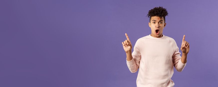 Portrait of shocked, speechless young hispanic man with dreads reacting to overwhelming shook news, gasping, drop jaw and staring concerned as pointing up at something astounding.