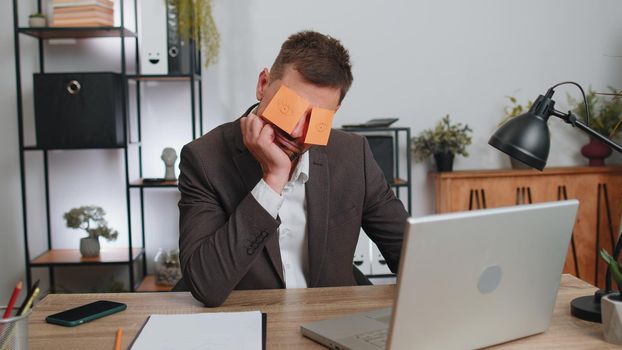 Inefficient tired businessman in suit working sleeping on laptop computer with eyes stickers on face at office workplace desk. Funny lazy manager freelancer man. Business people. Cheating to sleep