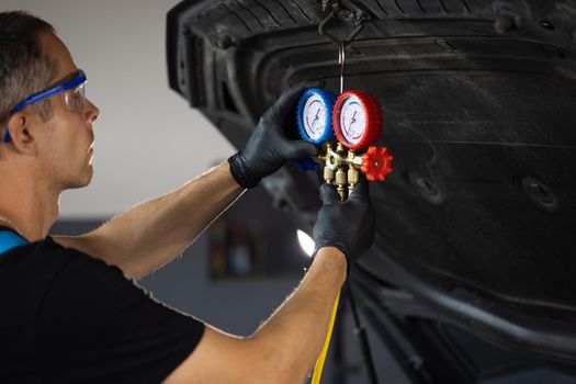 Car mechanic with manometer to fill the gas in the car air conditioning compressor. Service of checking the car air conditioner. Refrigerant recharge system.