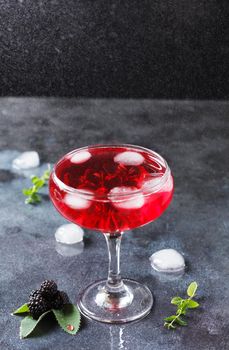 A glass of blackberry cocktail among small drops of water.
