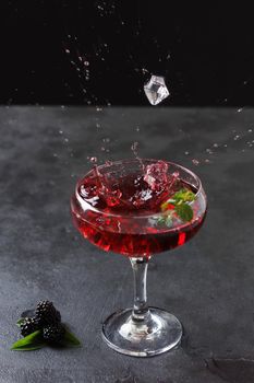 Ice falls into the glass, splashing around. Splash of blackberry smoothie