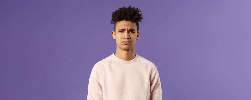 Close-up portrait of skeptical and gloomy, disappointed hispanic young man frowning upset, feel uneasy about bad idea, grimacing with disapproval, standing unhappy purple background.