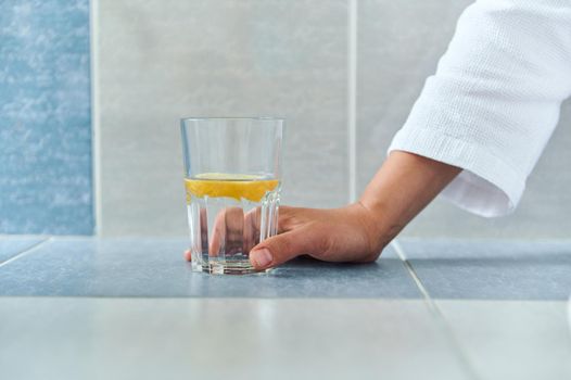 Close-up. Details: woman hand holding a drinking glass with fresh antioxidant lemon water. Morning drink for weight loss. Dieting. Healthy habits. Morning routine for good start to the day. Body care