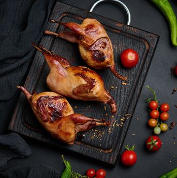 Frying carcasses of quails lie on a wooden board with vegetables, a black table