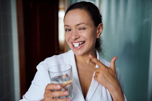 Close-up portrait of a happy multiethnic woman in white bathrobe, smiling at camera, taking medicine for antidepressant therapy. Mental health concept. Treating depression, stress and panic attacks