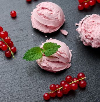 Pink ice cream balls on a black stone board, red currant berries nearby, top view