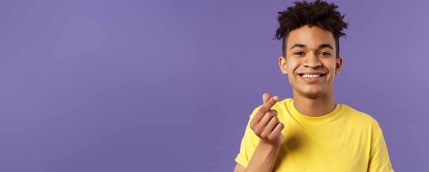 Lovely young romantic boyfriend, guy showing korean heart with fingers and smiling, like someone, being in love, show sympathy, standing purple background grinning upbeat.