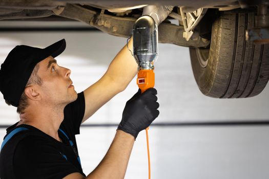 Caucasian male car mechanic checking car. Auto mechanic working underneath car lifting machine at the garage. Working in car repair shop and running small feminine business concept.