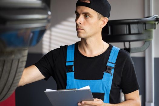 Automobile service, car mechanic. Car service employe inspect car. Mechanic inspects the car undercarriage way and makes a note on his inspection sheet. Modern workshop