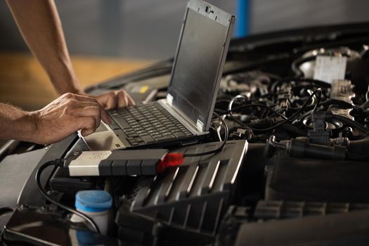 Automobile service, car mechanic. Auto mechanic uses a laptop while conducting diagnostics test. Specialist inspecting the vehicle in order to find broken components and errors in data logs.