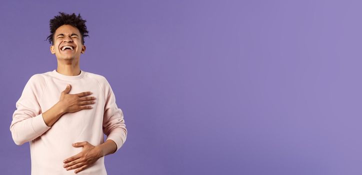 Portrait of cheerful, happy young hipster guy laughing out loud from hilarious joke, watching awesome stand-up performer, chuckle and touchign chest, bending backwards from laugh.