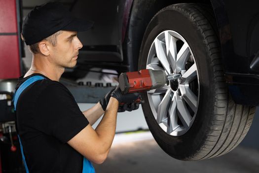 Repairman Works in a Modern Car Service. Specialists Removes the Wheel in Order to Fix a Component on a Vehicle. Mechanic is Unscrewing Lug Nuts with Pneumatic Impact Wrench.