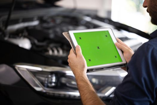 Mechanic running diagnostics software on tablet computer with green screen mockup chromakey. Unrecognizable vehicle service manager worker check and maintenance to repair the engine car in workshop.
