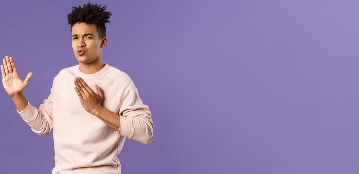 Portrait of funny and carefree young hispanic guy holding hands in martial arts attack pose, folding lips acting sassy and cool as imitating ninja, ready to defeat coronavirus, purple background.