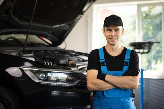 Portrait of car mechanic crossed arms in car workshop of service background . Concept: repair of machines, fault diagnosis, repair specialist, technical maintenance and on-board computer.