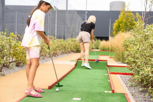 Mother playing with her cute daughter mini golf at outdoor playground