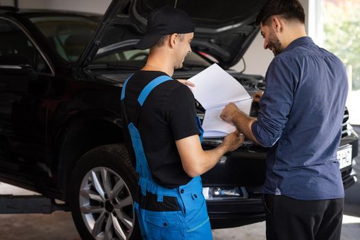 Mechanic and car owner signing paper at workshop. Customer and mechanic discuss upcoming car repair. Auto service, repair, deal and people concept.