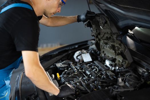 Car mechanic noting repair parts during open car hood engine repair at garage. Unrecognizable mechanic man open a car hood and check up the engine. Overheating of a car engine. Motor with open hood.
