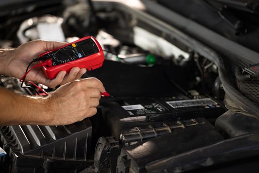 Mechanic doing car inspection, he is testing car battery with tester. Check battery voltage with electric multimeter. Man using multimeter to measure the voltage of the batteries.
